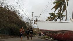 People walk by a damaged sail boat washed ashore after the area was hit by Hurricane Maria in Fajardo, Puerto Rico on September 20, 2017.
Maria made landfall on Puerto Rico, pummeling the US territory after already killing at least two people on its passage through the Caribbean. The US National Hurricane Center warned of "large and destructive waves" as Maria came ashore near Yabucoa on the southeast coast. / AFP PHOTO / Ricardo ARDUENGO