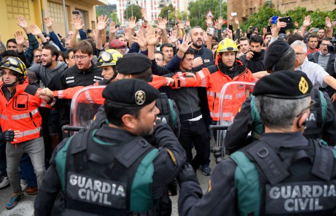 Bomberos forman una valla entre personas y agentes de la Guardia Civil afuera del centro de votación en Sant Julia de Ramis.