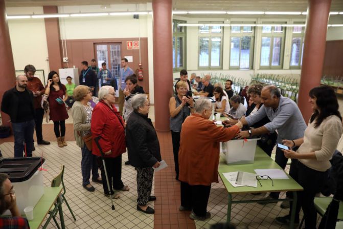 Una mujer vota mientras más personas hacen fila en un centro de votación en la escuela pública Escola Collaso I Gil de Barcelona.