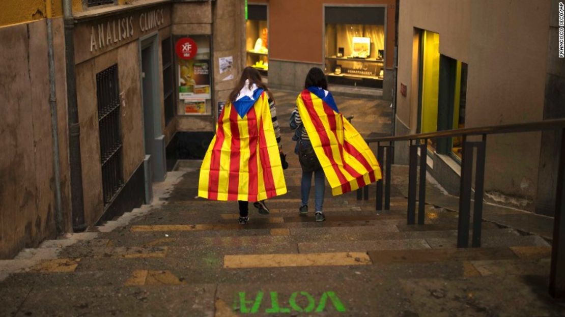 Dos mujeres caminan por el barrio antiguo de la ciudad de Girona, cubiertas por la bandera de Cataluña.