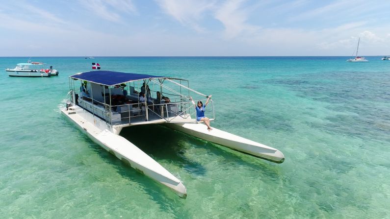 Piernas guindando. Era casi mágico ver Alejandra sentada en el catamarán en lo que se le llama la pasarela (lo que se convierte en el embarque y desembarque como una escalera). Para lograr esta toma con sus piernas guindando, deleitándose sobre el mar de postal, lo hicimos alzando el drone mientras navegamos las aguas idílicas en la provincia de La Romana. Nos retrasamos mucho en llegar a la Isla Catalina por esto de grabar con el drone porque los primeros intentos, el drone pasaba demasiado cerca de la cara de Alejandra, elevando tensiones de todos abordo del catamarán. Por un lado, Asdrúbal no podía ver dónde estaba el drone por el techo del barco. Por el otro, el drone luchaba contra el viento y la rapidez del barco. ¿Cómo lo solucionamos? Paramos el barco, así pudimos al menos controlar mejor el drone y lograr una serie de tomas dignas de la República Dominicana.