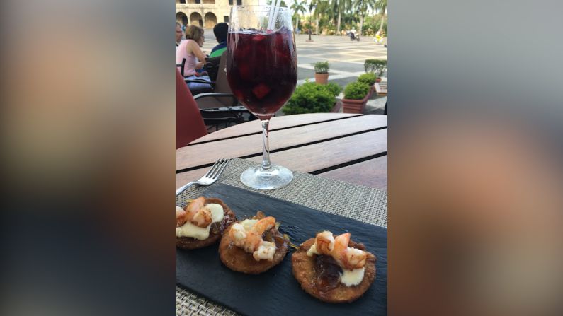 Tertulia al fresco en la Plaza de España. Cualquier viaje me queda incompleto si no le doy gusto al paladar. Por eso, tras haberlo visto varias veces mientras grababa la icónica Plaza de España, regresé para disfrutar de una tarde al fresco en el renombrado brasserie "Pat'e Palo" y de las creaciones del gran Chef Saverio Stassi. La tertulia incluía una copa de sangría y el aperitivo popular "Crispy Apple" hecha de fondue de parmesano, confitura de cebolla & jengibre, coronado con camarones salteados. Además de contemplar estos sabores me quedé pensando en el legado del sitio en dónde me encontraba… En este edificio se fundó la primera taberna de las Américas unos 500 años atrás, en 1505. Esta parada me satisface tanto el apetito como mi sed por la cultura.