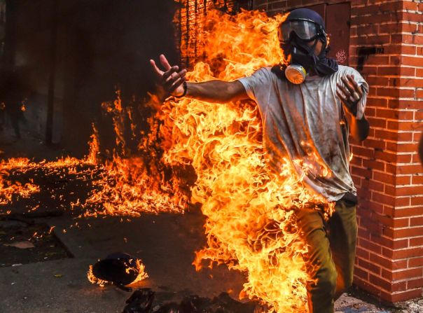 3 de mayo — Un manifestante queda envuelto en llamas durante las protestas antigubernamentales en Caracas, Venezuela. El hecho ocurrió cuando las personas que protestaban se enfrentaron a la Policía y explotó el tanque de gasolina de una moticicleta de las autoridades. Otras fotos de la escena registraron al hombre siendo atendido con quemaduras en su cuerpo.