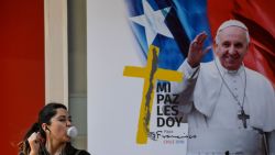 A woman blows a bubble with chewing gum, as she walks past a welcome poster with the image of Pope Francis, ahead of his upcoming visit to Santiago on January 11, 2018.
Pope Francis will be visiting Chile from January 15 to 18. / AFP PHOTO / Martin BERNETTI