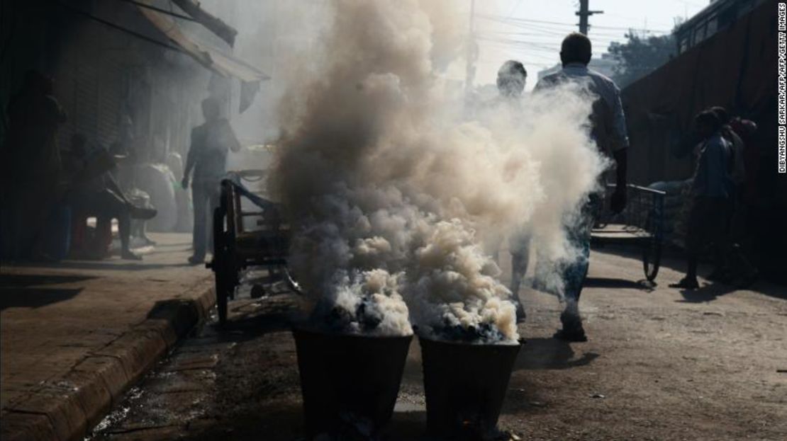 Vecinos de la India caminan cuando un denso humo sale de los "chulahs" (hornos de carbón tradicionales) colocados al costado de una concurrida vía en Kolkata, en febrero de 2018.