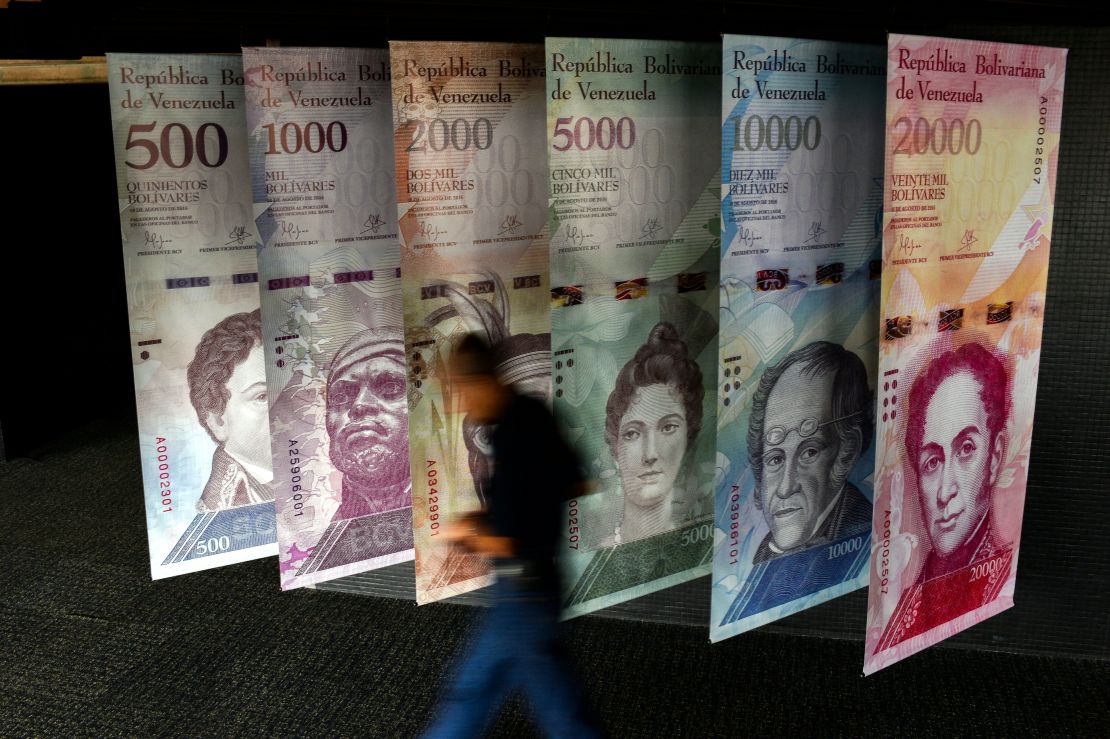 Un hombre camina frente a pancartas que representan la moneda de Venezuela, el Bolívar, en el Banco Central de Venezuela.