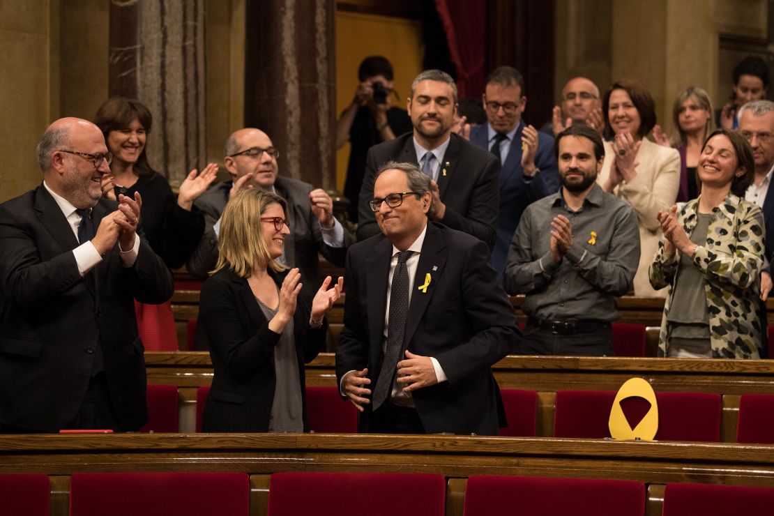 Quim Torra recibe el aplauso de la bancada tras conseguir ser nombrado presidente de la Generalitat de Cataluña. A su lado, uno de los asientos vacíos de los diputados ausentes, señalado con un lazo amarillo como símbolo del independentismo.