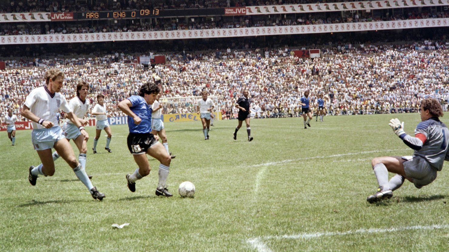 Diego Armando Maradona supera al defensor inglés Terry Butcher (izq.) antes de regatear al guardameta Peter Shilton (der.) y anotar el considerado "Gol del siglo durante el partido de cuartos de final de la Copa del Mundo entre Argentina e Inglaterra el 22 de junio de 1986 en la Ciudad de México. Argentina avanzó a las semifinales con una victoria de 2-1. Crédito: STAFF / AFP / Getty Images.