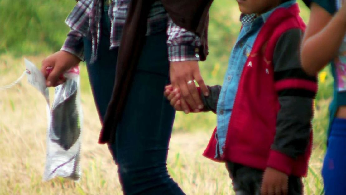 Imagen de un niño de la mano de un adulto, cerca de la frontera entre Estados Unidos y México.