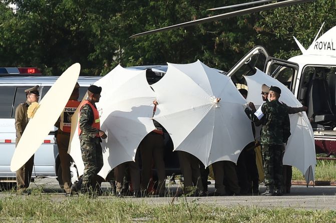 La policía y el personal militar usaron sombrillas para cubrir una camilla cerca de un helicóptero y una ambulancia en las operaciones de rescate de los niños.