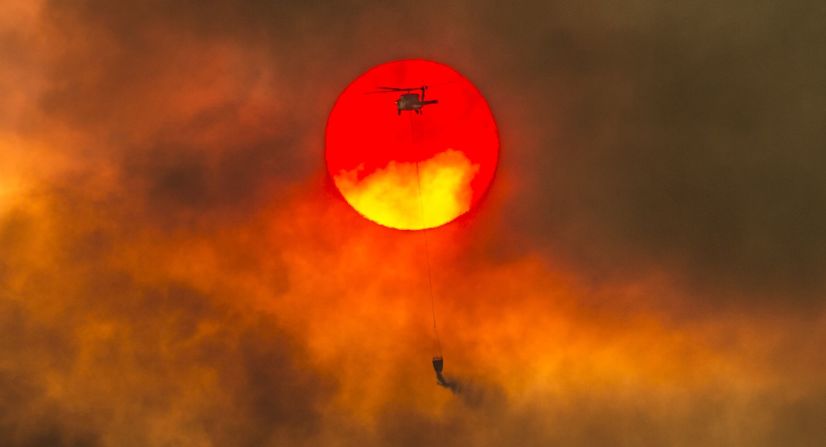 Un helicóptero contra incendios vuela mientras el sol se pone sobre las llamas, cerca de Redding.