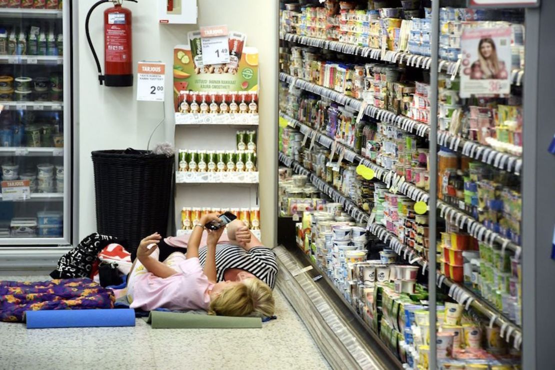 Mujeres en Helsinki, Finlandia, se toman una fotografía junto a repisas con sistema de enfriamiento en una tienda local que permite a los clientes refrescarse