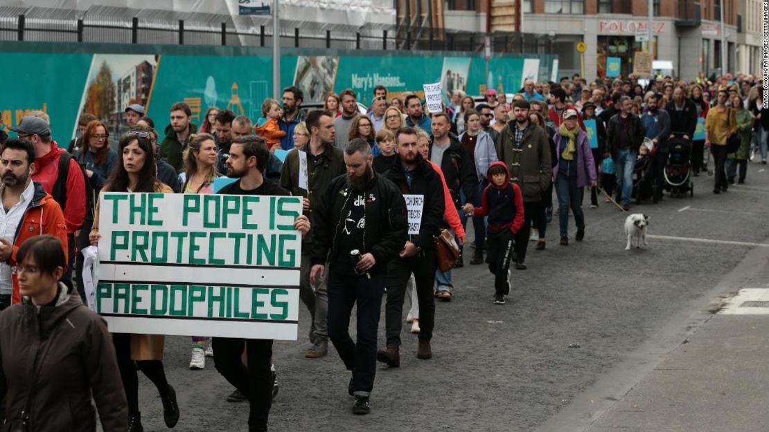 Ailbhe O'Rourke y Fionn Dally sostienen un cartel que dice: "El papa protege a los pedófilos" en protesta por los casos de sacerdotes que cometieron abusos sexuales.