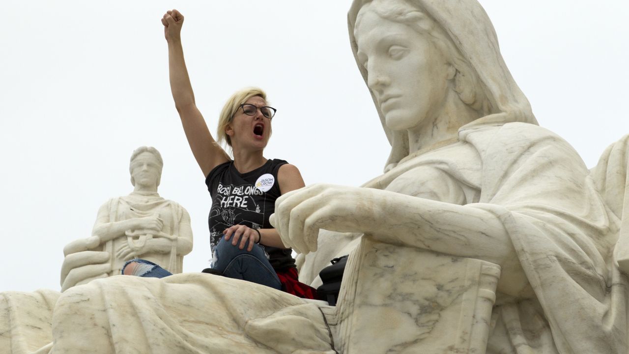 TOPSHOT - Demonstrator Jessica Campbell-Swanson of Denver, stands on the lap of the "Contemplation of Justice" statue as protestors take the steps of the US Supreme Court protesting against the appointment of Supreme Court nominee Brett Kavanaugh at Capitol Hill in Washington DC, on October 6, 2018. (Photo by Jose Luis Magana / AFP)