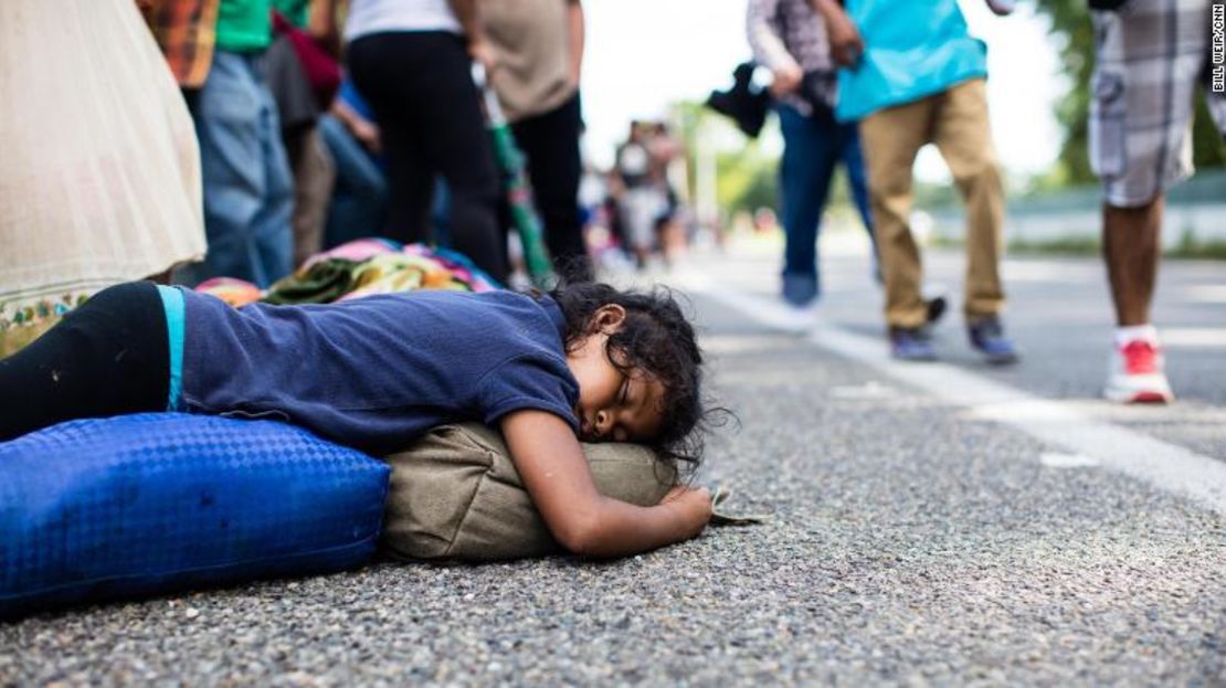 Una niña duerme al lado de la carretera mientras sus compañeros migrantes pasan caminando