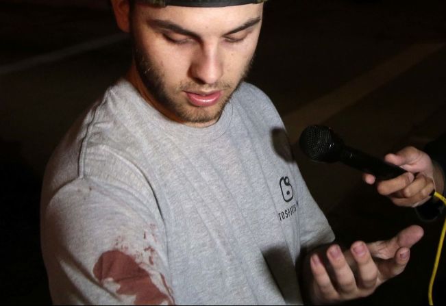 Matt Wennerstorm, vistiendo aún su camiseta manchada de sangre, habla con la prensa afuera del bar.