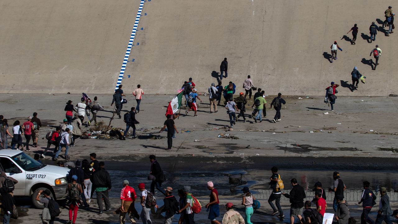 TOPSHOT - Central American migrants -mostly from Honduras- cross the shallow concrete waterway of the bordering Tijuana River as they try to reach the El Chaparral border crossing point in Tijuana, Baja California State, Mexico, on November 25, 2018. - US officials closed the San Ysidro crossing point in southern California on Sunday after hundreds of migrants, part of the "caravan" condemned by President Donald Trump, tried to breach a fence from Tijuana, authorities announced. (Photo by GUILLERMO ARIAS / AFP)