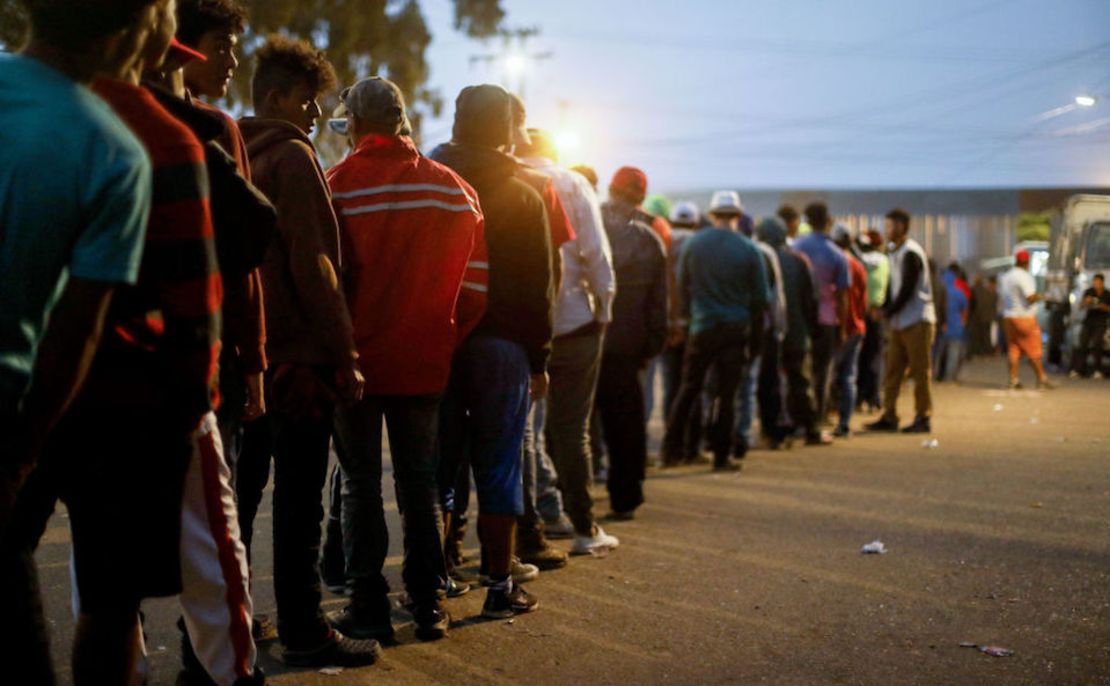 Migrantes en Tijuana hacen fila para recibir comida en un refugio temporal.