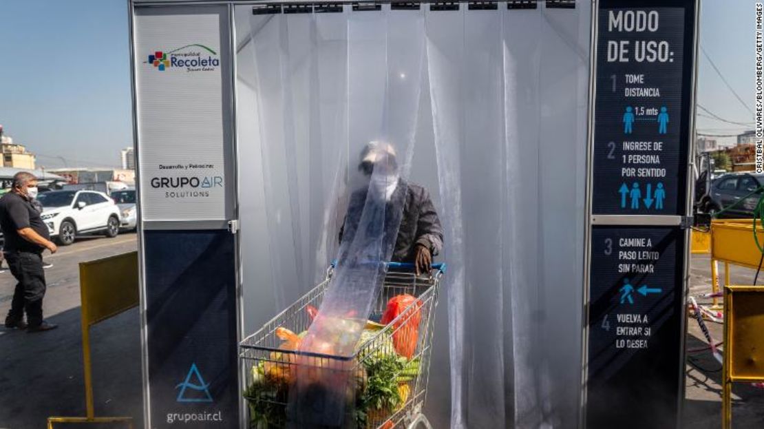 Una persona usando mascarilla empuja un carrito del mercado a través de un cuarto de descontaminación en el mercado de frutas y verduras de La Vega Central en Santiago, Chile.