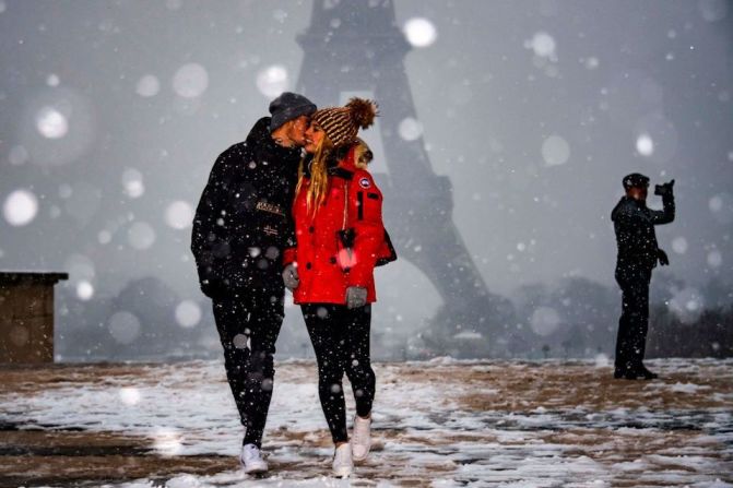 Una pareja camina bajo la nieve frente a la Torre Eiffel.