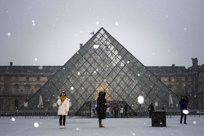 Turistas toman fotos de la pirámide de cristal en el museo de Louvre, en medio de la nevada.