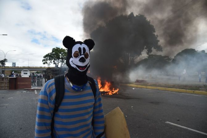 Un manifestante enmascarado se para frente a una van incendiada por manifestantes de la oposición venezolana durante las protestas del 23 de enero.