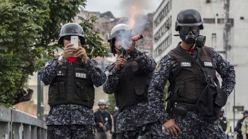 Un agente de la Policía Nacional dispara gases lacrimógenos contra los manifestantes en Caracas mientras otro captura la escena con un teléfono celular. (Rayner Pena / picture alliance via Getty Images).