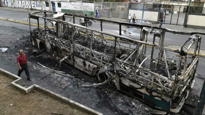 Un hombre camina cerca a un autobús que había sido incendiado en Caracas. (Luis Robayo / AFP / Getty Images).