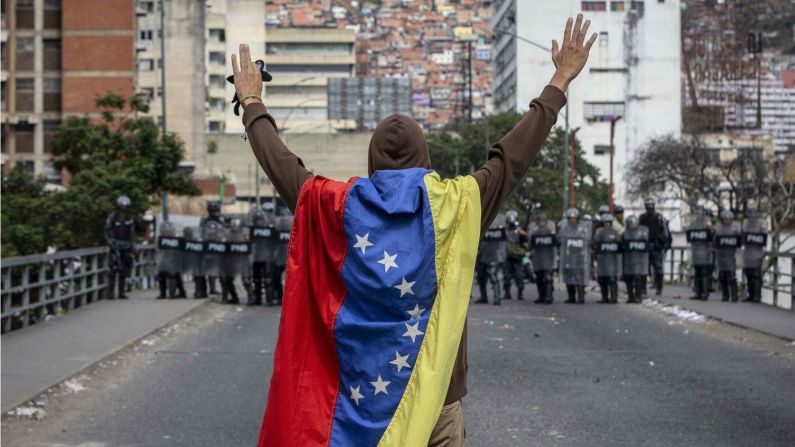 Un hombre envuelto en una bandera venezolana alza sus brazos frente a las fuerzas militares en medio de antigubernamentales en Caracas el 23 de enero de 2019. (Rayner Pena / imagen alianza vía Getty Images).