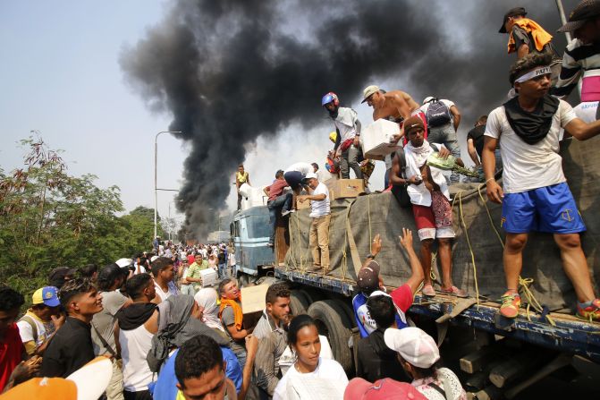 La gente intenta rescatar parte de la ayuda humanitaria después de que un camión se incendiaria en el puente Santander.