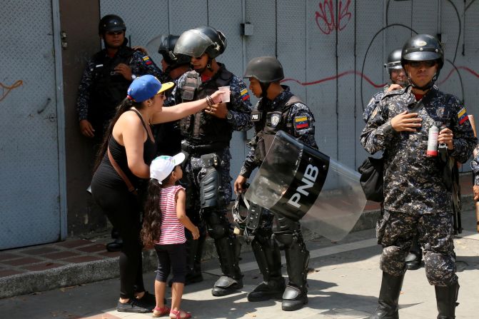 Una mujer que participa en la protesta en rechazo al régimen de Nicolás Maduro ofrece un vaso con agua a un agente de la Policía Nacional Bolivariana, PNB.