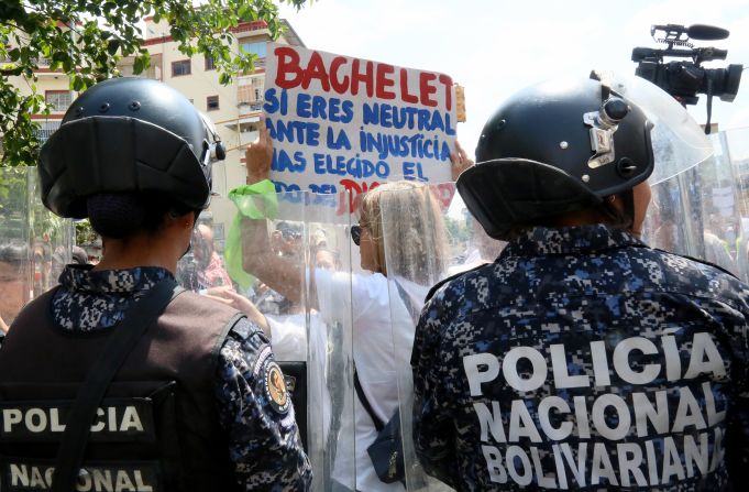 Una mujer sostiene un cartel frente a una línea de agentes de de la Policía Nacional Bolivariana, PNB.