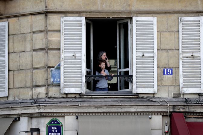 Una mujer y un niño junto a la ventana de un apartamento mientras observan cómo las llamas arrasan el techo de la Catedral de Notre-Dame en París el 15 de abril de 2019. Crédito: GEOFFROY VAN DER HASSELT / AFP / Getty Images