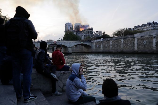 People look at smoke and flames rising during a fire at the landmark Notre-Dame Cathedral in central Paris on April 15, 2019. - A fire broke out at the landmark Notre-Dame Cathedral in central Paris, potentially involving renovation works being carried out at the site, the fire service said. (Photo by Thomas SAMSON / AFP).