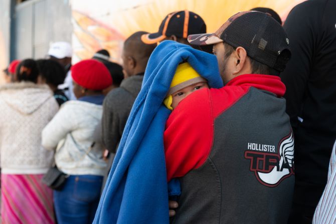 José Manuel Salinas, de Acapulco, Guerrero, sostiene al bebé de su amigo mientras espera en la fila para que lo vea una enfermera. (KHN).