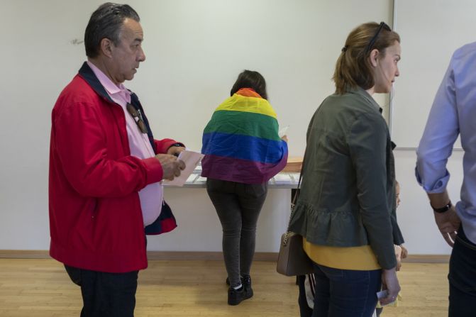 Una mujer vestida con una bandera del arco iris, símbolo del movimiento LGBT, prepara su voto cuando la gente hace cola en Pozuelo de Alarcón, en Madrid.