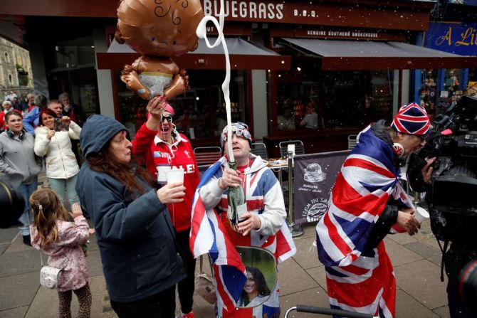 Fanáticos de la realeza celebran con una botella de champaña el nacimiento del primer hijo del príncipe Enrique y Meghan Markle.