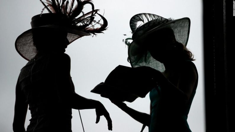 Mujeres usando sombreros extravagantes leen un folleto antes del Derby de Kentucky.