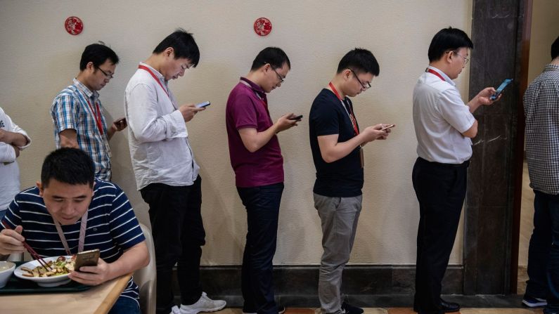 Empleadosde Huawei miran sus teléfonos inteligentes mientras hacen fila para almorzar en el campus de Dongguan.