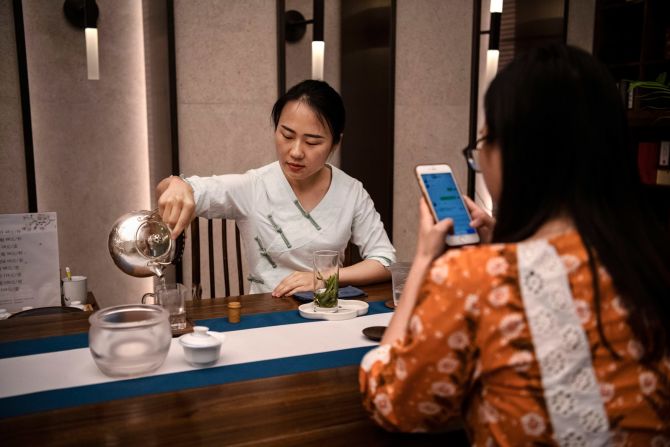 Una empleada mira su teléfono inteligente mientras una mujer sirve té en un café en el campus Bantian de la compañía en Shenzhen.