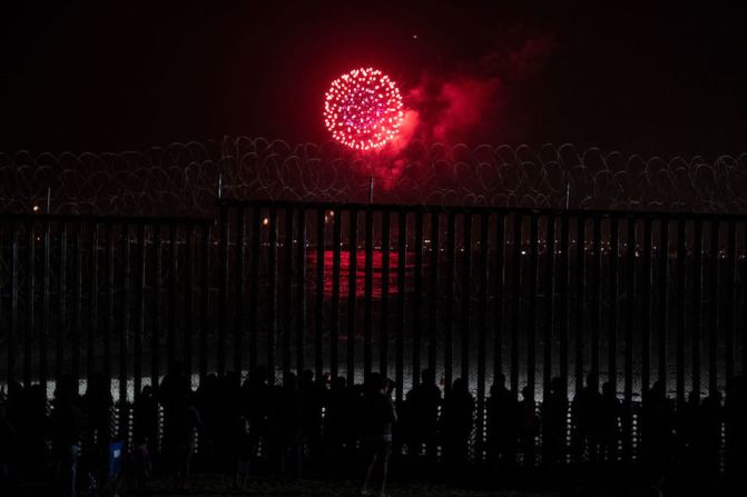 Personas en Tijuana miran los fuegos artificiales de 4 de julio sobre San Diego a través de la valla fronteriza que separa a Estados Unidos y México.