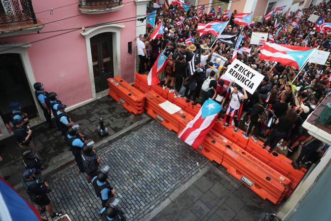 Los manifestantes protestan frente a policías que impiden el paso en una calle que lleva a La Fortaleza, la residencia del gobernador.