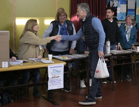 El presidente y candidato presidencial de Argentina, por el partido Juntos por el Cambio, Mauricio Macri , se da la mano con un funcionario electoral antes de votar.