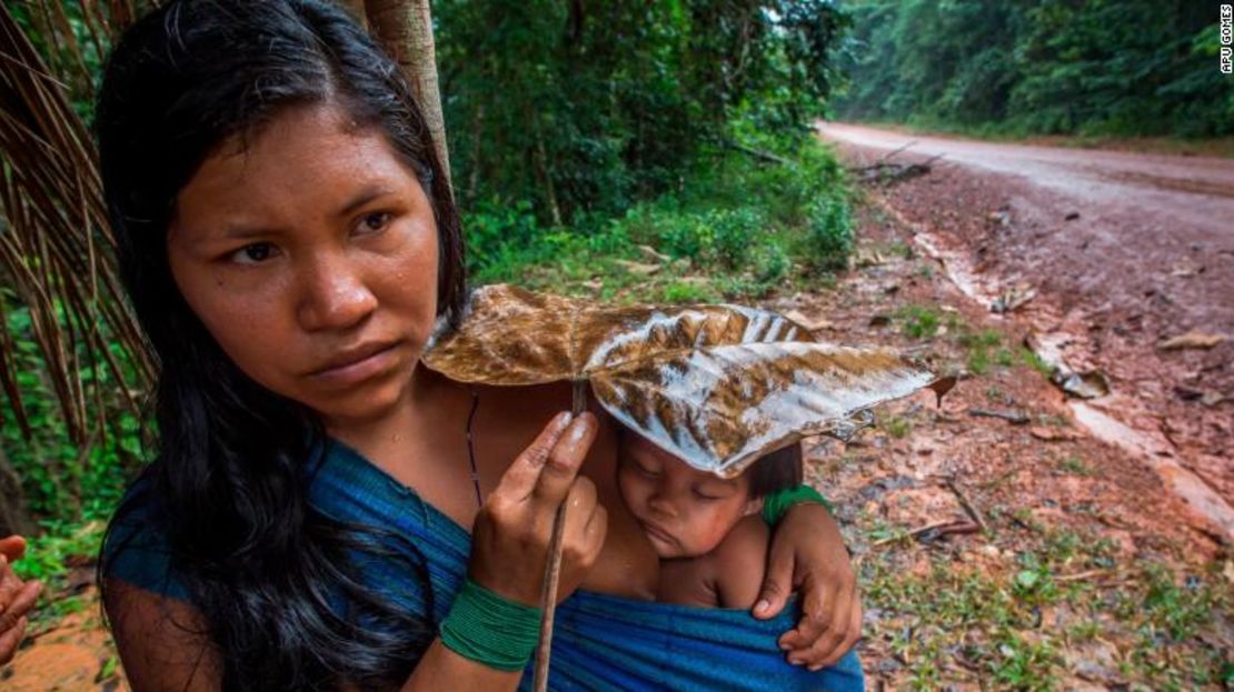 Karuwaniru Waiaipi protege a su pequeño hijo de la lluvia con una hoja, mientras camina por la carretera BR-210 Perimetral Norte cerca del pueblo de Aramira.