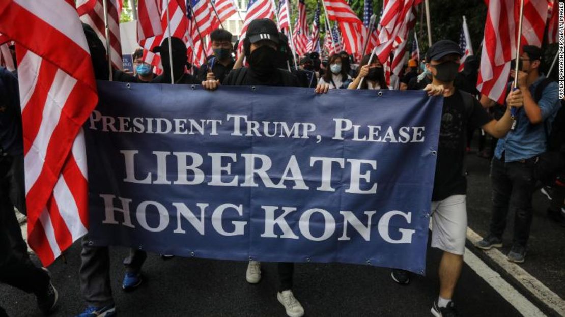 Los manifestantes sostienen una pancarta y agitan banderas nacionales de EE.UU. mientras marchan al Consulado de EE.UU. en Hong Kong.