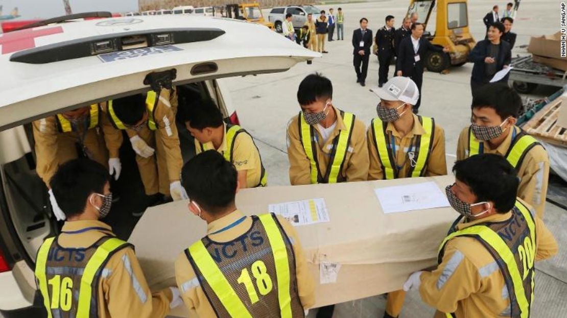 Personal aeroportuario carga un ataúd hacia una ambulancia en Hanoi.