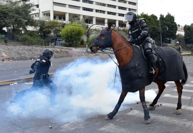 Un agente antidisturbios patea una lata de gas lacrimógeno para alejarla del caballo de un agente de la policía montada.