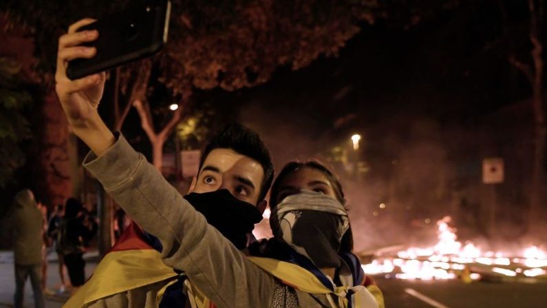 Dos manifestantes se toman una selfie mientras atrás arden las barricadas en Barcelona. (Photo by LLUIS GENE / AFP).