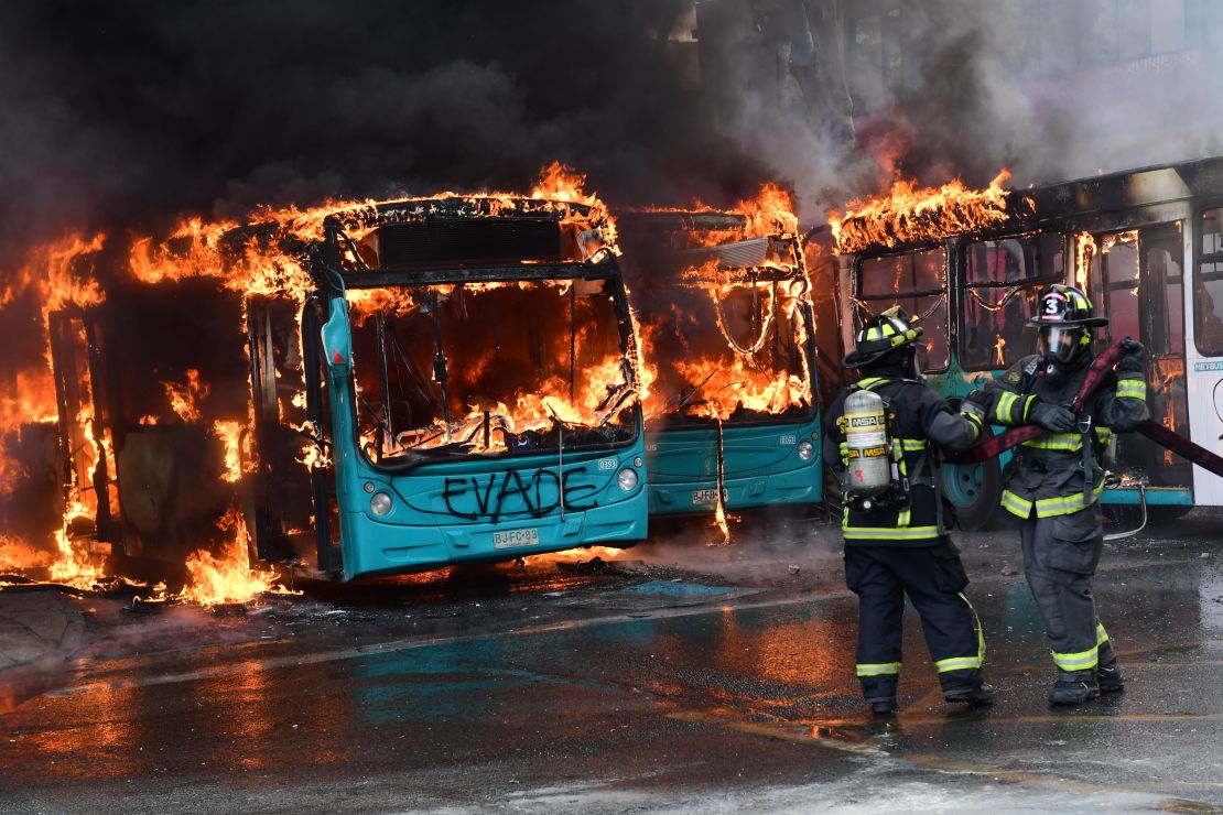 Bomberos chilenos extinguen las llamas de un autobús que fue quemado durante las protestas.