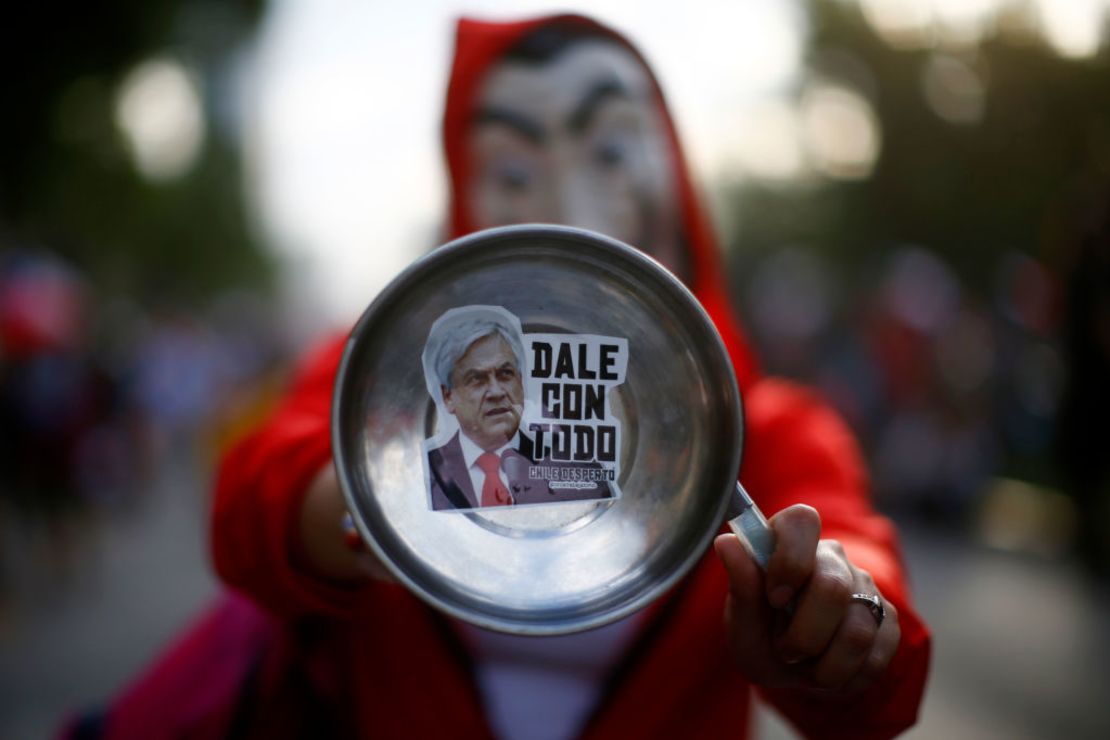 Un manifestante enmascarado sostiene una olla que representa al presidente chileno Sebastián Piñera donde dice "Dale con todo".